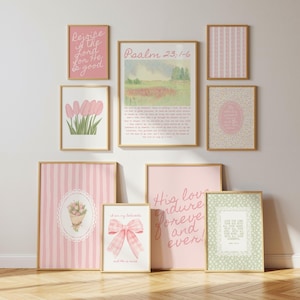 May include: A collection of framed art prints in various sizes and designs. The prints feature floral illustrations, inspirational quotes, and scripture verses in soft pink, green, and gold tones. The artwork is displayed on a white wall with a wooden floor.