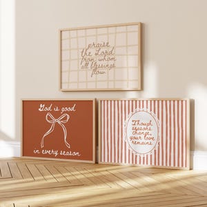 May include: Three framed art prints with inspirational quotes. The top print has a grid pattern and the text "praise the Lord from whom all blessings flow." The middle print is orange with the text "God is good in every season." The bottom print has vertical stripes and the text "Though seasons change, your love remains."