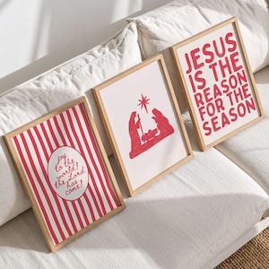 May include: Three framed Christmas art prints with wooden frames. The prints feature red and white designs, including vertical stripes, a nativity scene, and the text "JESUS IS THE REASON FOR THE SEASON". One print reads "Joy to the world! the Lord has come!"