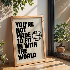 May include: A framed print with a beige background and black text that reads "You're not made to fit in with the world". A black globe icon is next to the text.