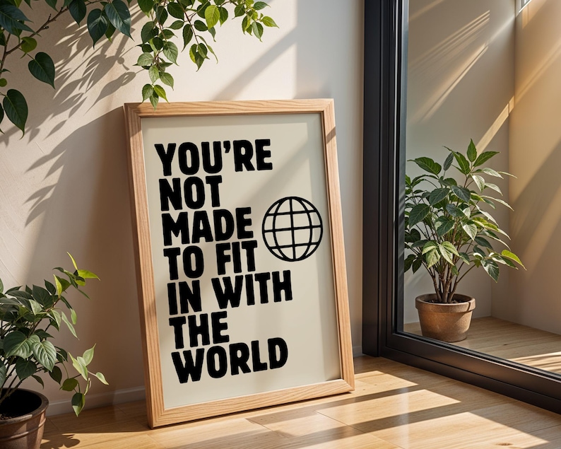 May include: A framed print with a beige background and black text that reads "You're not made to fit in with the world". A black globe icon is next to the text.