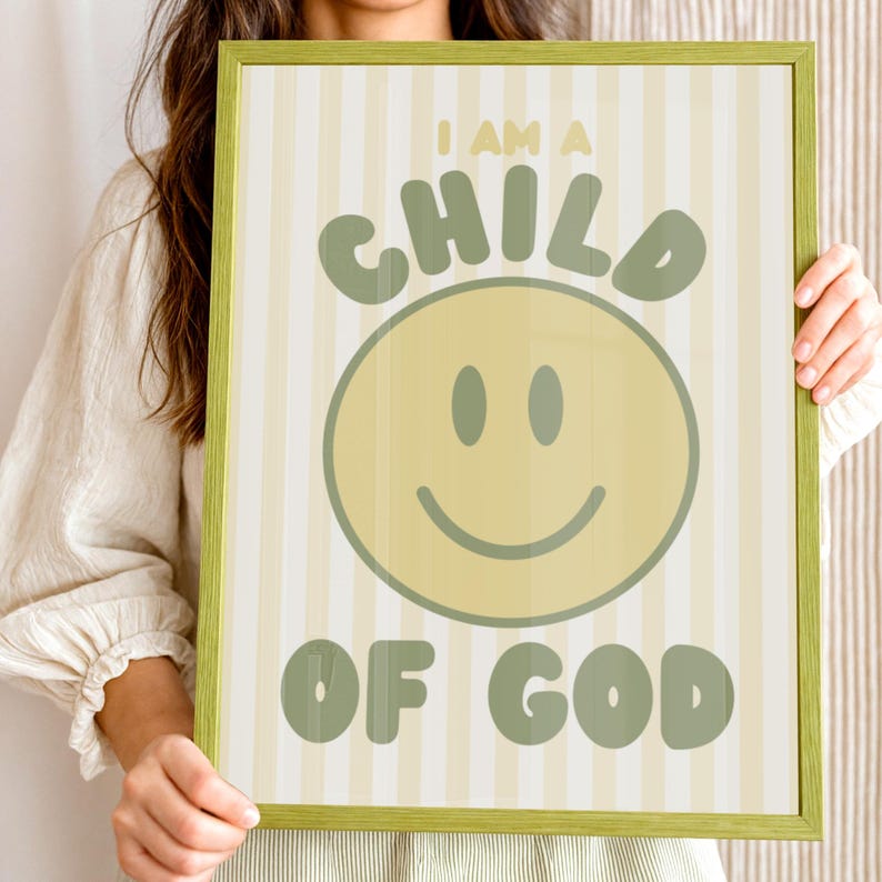May include: A framed print with a green border features the text "I AM A CHILD OF GOD" in green lettering. A large yellow smiley face is centered below the word "CHILD". The background has vertical stripes in light yellow and white.