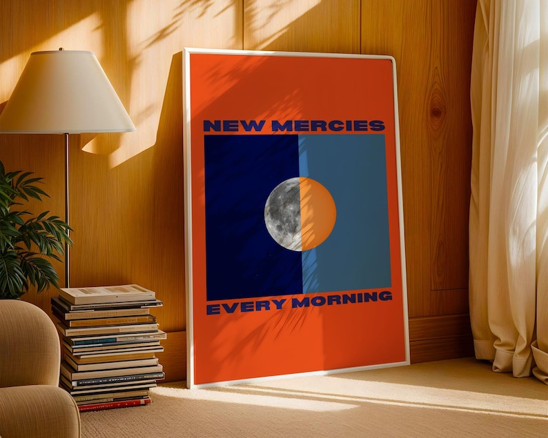 May include: A poster with an orange background and a blue and black rectangle in the centre. The rectangle has a half moon in it. The text "NEW MERCIES EVERY MORNING" is printed in blue on the poster.