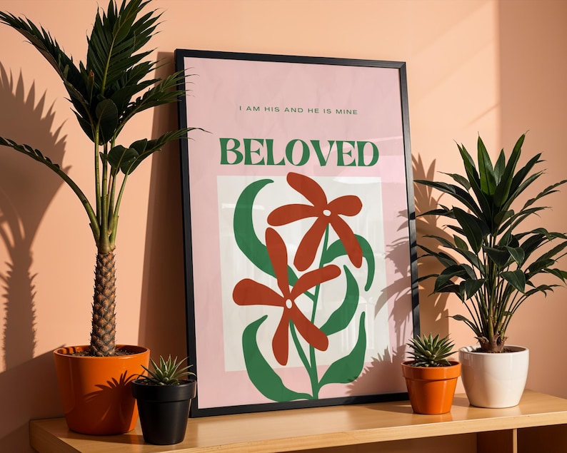 May include: A pink and green poster with a black frame. The poster features a stylized illustration of two red flowers with green leaves. The text on the poster reads "I am his and he is mine, BELOVED".