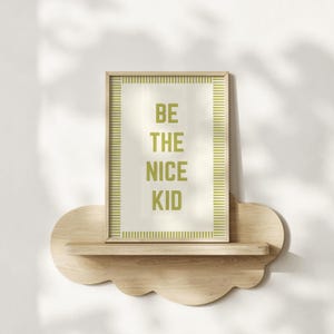 May include: A framed print with the text "BE THE NICE KID" in green letters. The print is set against a cream background and framed with a green striped border. It rests on a cloud-shaped wooden shelf.
