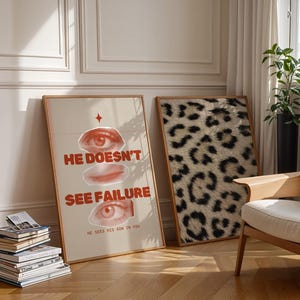 May include: Two framed posters on a white wall. The poster on the left features a red and white graphic with the text "He doesn't see failure. He sees his son in you." The poster on the right features a black and white animal print.