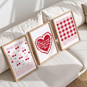 Op de afbeelding: Drie ingelijste kunstdrukken met houten frames. De prints hebben rode ontwerpen en tekst op een witte achtergrond. Eén print heeft kersen, een andere een hart en de derde een rood-wit geruit patroon. De tekst bevat "PSALMS" en bijbelverzen.