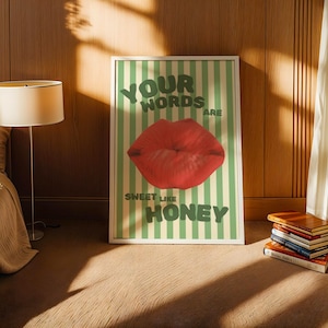May include: A framed print with a green and white striped background. The print features a red lip with the text "Your words are sweet like honey".