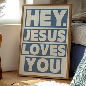 Op de afbeelding: Een ingelijste poster met een blauwe achtergrond en witte tekst die "HEY. JESUS LOVES YOU." luidt.