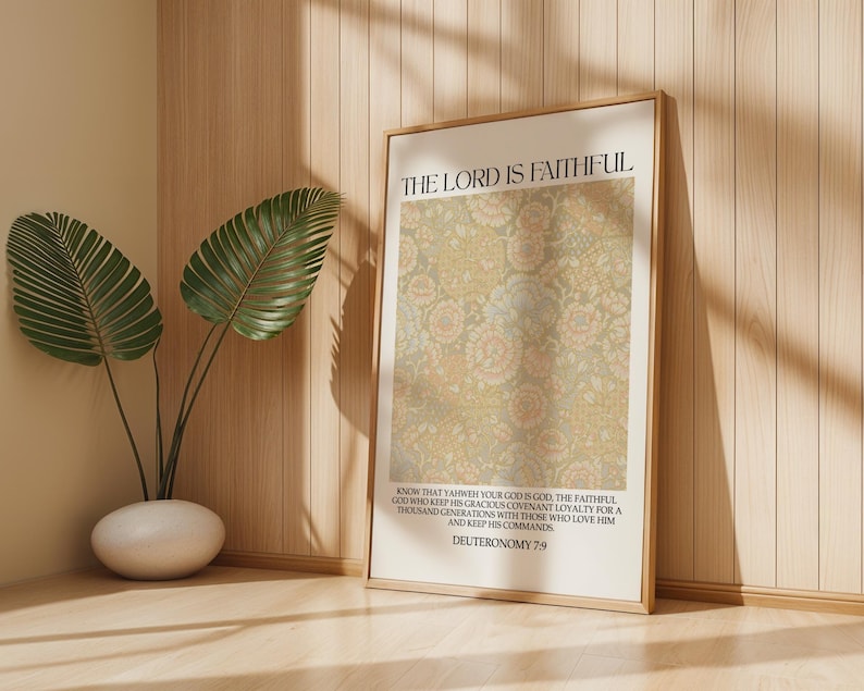May include: A framed print with the text "THE LORD IS FAITHFUL" and a floral pattern in beige and pink. The print is displayed on a light wood surface, next to a potted plant with large green leaves.