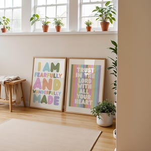 May include: Two framed art prints with inspirational quotes. One reads "I AM FEARFULLY AND WONDERFULLY MADE" in colorful bubble letters. The other says "TRUST IN THE LORD WITH ALL YOUR HEART" in pastel stripes. A small wooden stool and potted plants are also visible.