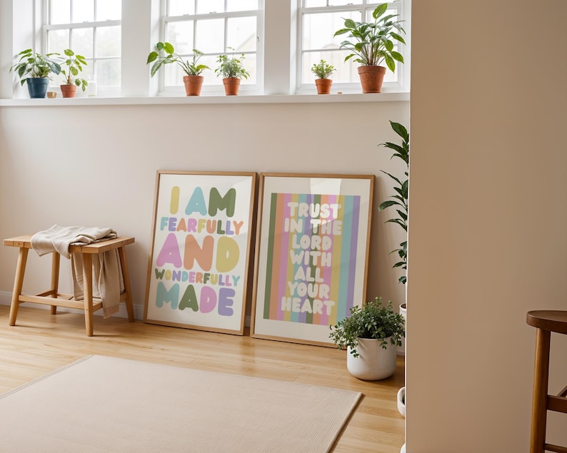 May include: Two framed art prints with inspirational quotes. One reads "I AM FEARFULLY AND WONDERFULLY MADE" in colorful bubble letters. The other says "TRUST IN THE LORD WITH ALL YOUR HEART" in pastel stripes. A small wooden stool and potted plants are also visible.