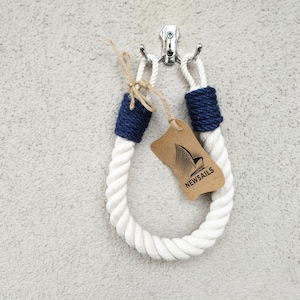 May include: White rope doorstop with blue rope ends and a brown tag that says "NEWSAILS".