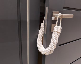 May include: A white rope doorstop with a braided design hangs on a gray door with a silver door handle.