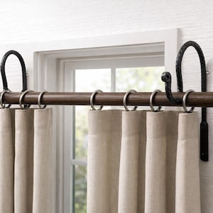 May include: A dark brown wooden curtain rod with black metal brackets and silver rings holding beige curtains. The rod is mounted above a window with a white frame, creating a rustic and elegant look for home decor.