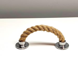 Op de afbeelding: Een natuurlijke touwgreep met een bruine kleur en zilveren metalen eindkappen. Het touw is gedraaid en heeft een lichte boogvorm.