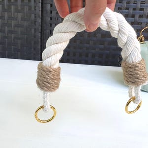 May include: A white rope handbag handle with jute twine accents and gold-colored metal rings. The handle is arched and appears to be new. A light green handbag is visible in the background.