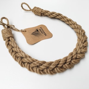 May include: A thick, braided rope curtain tieback in a natural brown color. The rope is tied into a loop at each end. The tieback is labeled "NEWSAILS".