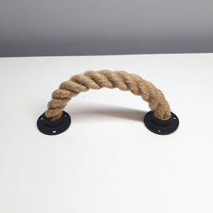 Puede incluir: Un tirador de cuerda rústico de color beige natural. La gruesa cuerda está sujeta a dos placas de montaje de metal negro. Este tirador es adecuado para cajones, armarios u otros muebles.