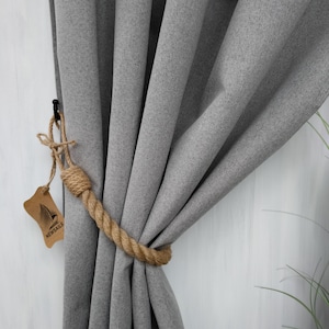Pode incluir: Cortina cinza com um amarrador de corda marrom. O amarrador &eacute; feito de corda natural e tem uma pequena etiqueta com a palavra "NEWSAILS" nela.