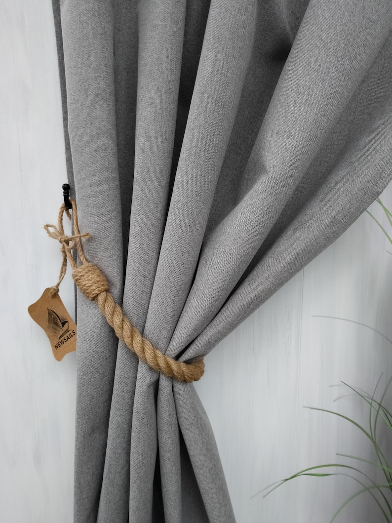 Pode incluir: Cortina cinza com um amarrador de corda marrom. O amarrador &eacute; feito de corda natural e tem uma pequena etiqueta com a palavra "NEWSAILS" nela.