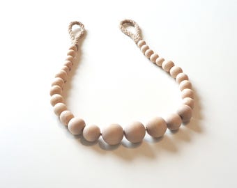 May include: A decorative wooden bead garland with a natural finish. The garland features various sized round beads strung together with a natural rope loop at each end. The beads are light brown and arranged in a curved shape.
