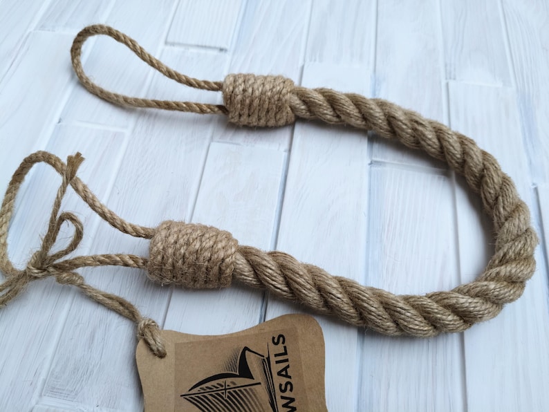 Pode incluir: Um amarrador de cortina de corda grossa e natural com duas al&ccedil;as em uma extremidade. A corda &eacute; feita de fibras naturais e tem um visual r&uacute;stico. A corda &eacute; amarrada em um n&oacute; na outra extremidade. A corda tem cerca de 76 cm de comprimento.