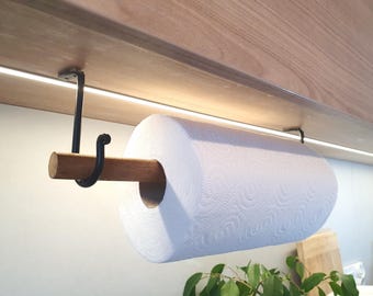 Könnte beinhalten: Ein Papierhandtuchhalter mit einer Holzstange und schwarzen Metallhalterungen, montiert unter einem Holzschrank. Eine Rolle weißer Papierhandtücher ist eingesetzt. Der Halter ist für den einfachen Gebrauch in der Küche konzipiert.