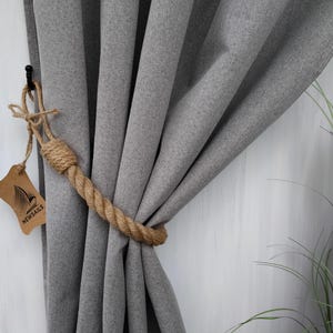 Pode incluir: Cortinas cinzas com um amarrador de corda. O amarrador &eacute; feito de corda natural e tem uma etiqueta castanha com o texto "NEWSAILS".