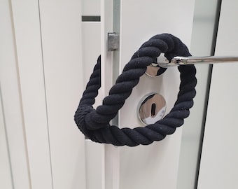 May include: A black rope door handle wrap is looped around a silver door handle and a white door. The thick rope is tightly wound, creating a circular design. The door has a silver keyhole cover.