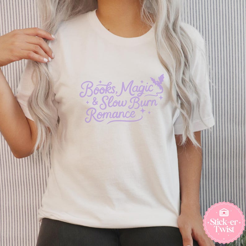 Puede incluir: Camiseta blanca con el texto "Books, Magic & Slow Burn Romance" en morado claro. El dise&ntilde;o incluye un murci&eacute;lago y estrellas. Una prenda casual.