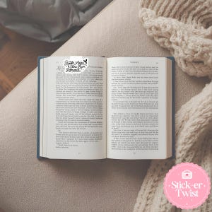 Puede incluir: Un libro abierto con tapas azules, texto en las p&aacute;ginas y un marcador que dice "Books, Magic & Slow Burn Romance". Una pegatina rosa con el texto "Stick-er Twist" est&aacute; en la esquina inferior derecha.