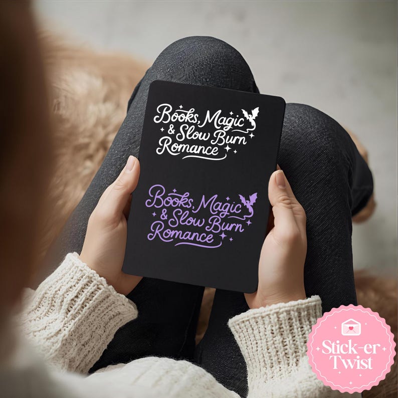 Puede incluir: Un cuaderno negro con el texto "Books, Magic & Slow Burn Romance" en blanco y morado. El cuaderno est&aacute; sostenido en las manos de alguien, con una pegatina en la esquina inferior derecha que dice "Stick-er Twist".