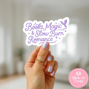 Puede incluir: Una pegatina blanca con el texto "Books, Magic & Slow Burn Romance" en escritura morada, con una ilustraci&oacute;n de un murci&eacute;lago. La pegatina est&aacute; sujeta por una mano con anillos dorados y esmalte de u&ntilde;as iridiscente. Una pegatina rosa con el texto "Stick-er Twist" est&aacute; en la esquina inferior derecha.