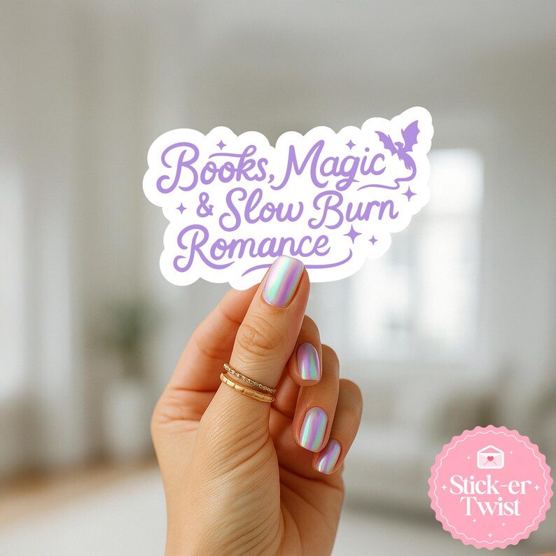 Puede incluir: Una pegatina blanca con el texto "Books, Magic & Slow Burn Romance" en escritura morada, con una ilustraci&oacute;n de un murci&eacute;lago. La pegatina est&aacute; sujeta por una mano con anillos dorados y esmalte de u&ntilde;as iridiscente. Una pegatina rosa con el texto "Stick-er Twist" est&aacute; en la esquina inferior derecha.