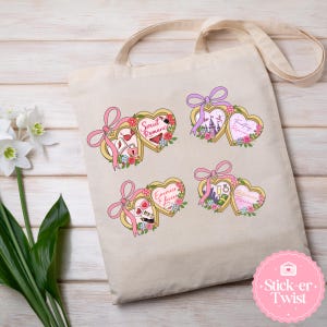 Puede incluir: Un bolso tote beige con cuatro dise&ntilde;os en forma de coraz&oacute;n con lazos rosas y detalles florales. Cada coraz&oacute;n contiene un gr&aacute;fico y texto diferente, incluyendo "Smut Romance", "Fantasy Romance", "Enemies Lovers" y "Billionaire Romance".