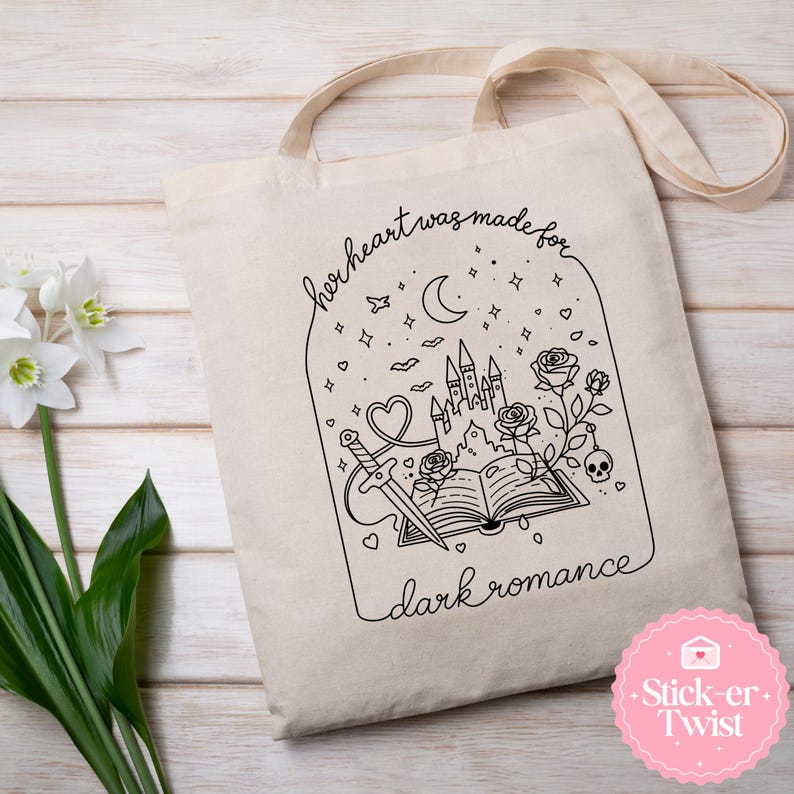 May include: Beige canvas tote bag with a black line art design. The design features a castle, sword, roses, and the text "her heart was made for dark romance". The bag has long, beige straps.