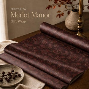Könnte beinhalten: Eine Rolle dunkelburgunderfarbenes Geschenkpapier mit einem sich wiederholenden Muster aus kleinen, filigranen Blumen- und Blattmotiven in gedeckten Rot- und Brauntönen. Der Text "FROST & Fig Merlot Manor Gift Wrap" steht oben links.