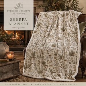 May include: A sherpa blanket featuring a cream-colored base with a repeating botanical print of brown and green pine branches and foliage. The text on the image reads EVERGREEN RESERVE by Frost & Fig SHERPA BLANKET.
