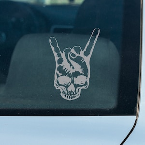 May include: A silver car with a skull and hand making the rock and roll sign on the back window.