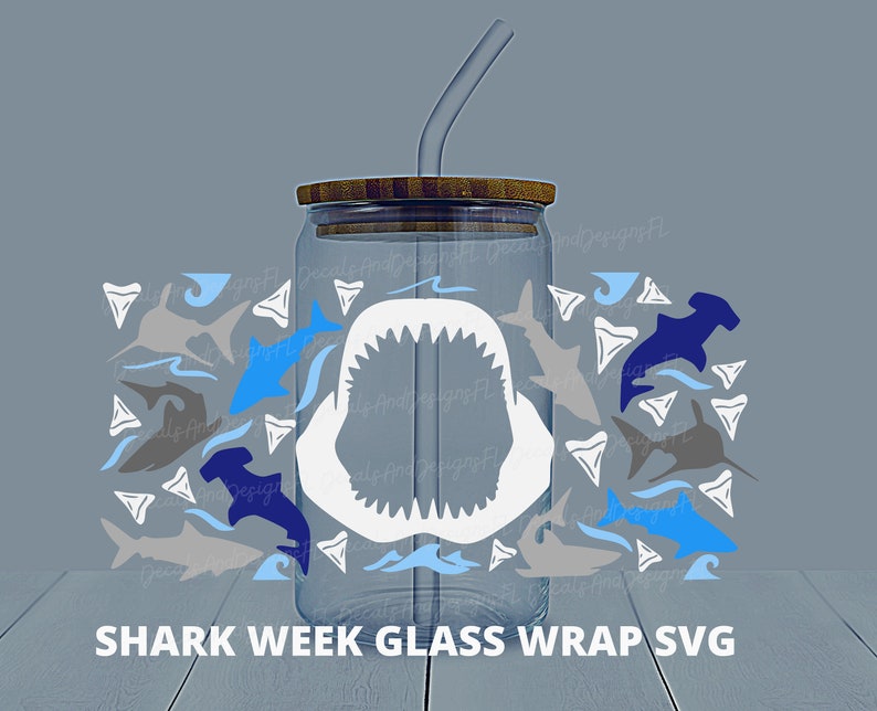 May include: A clear glass tumbler with a brown lid and a straw. The tumbler is decorated with a white shark mouth and a variety of blue, gray, and white shark silhouettes, including hammerhead sharks and shark teeth. The text "SHARK WEEK GLASS WRAP SVG" is printed below the tumbler.