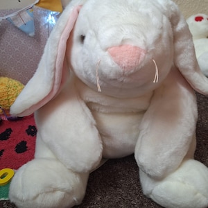 May include: A large, white plush bunny rabbit with long, floppy ears and a pink nose and inner ears. The stuffed animal has a soft, fluffy texture and is sitting upright. The bunny has long whiskers and is a classic children's toy.