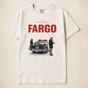 May include: Cream-colored t-shirt with the word "FARGO" in red block letters. Below the word "FARGO" is a black and white illustration of a police car with two figures. The text "FROM COEN BROTHERS" is above the word "FARGO".