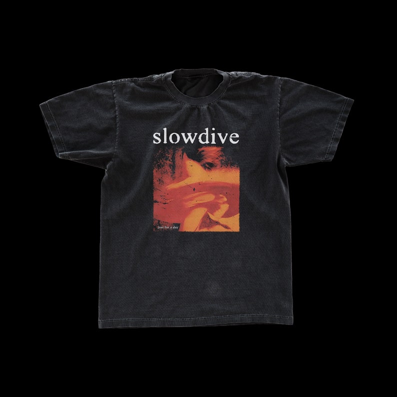 Puede incluir: Camiseta negra con un gr&aacute;fico descolorido naranja y rojo de la cara de una persona y el texto "slowdive" y "just for a day".
