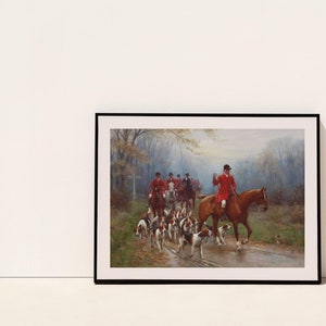 May include: Framed print of a hunting scene. A group of riders in red coats on horseback lead a pack of hounds along a path. The artwork has a classic, traditional style, with muted colors and a focus on the riders and dogs.