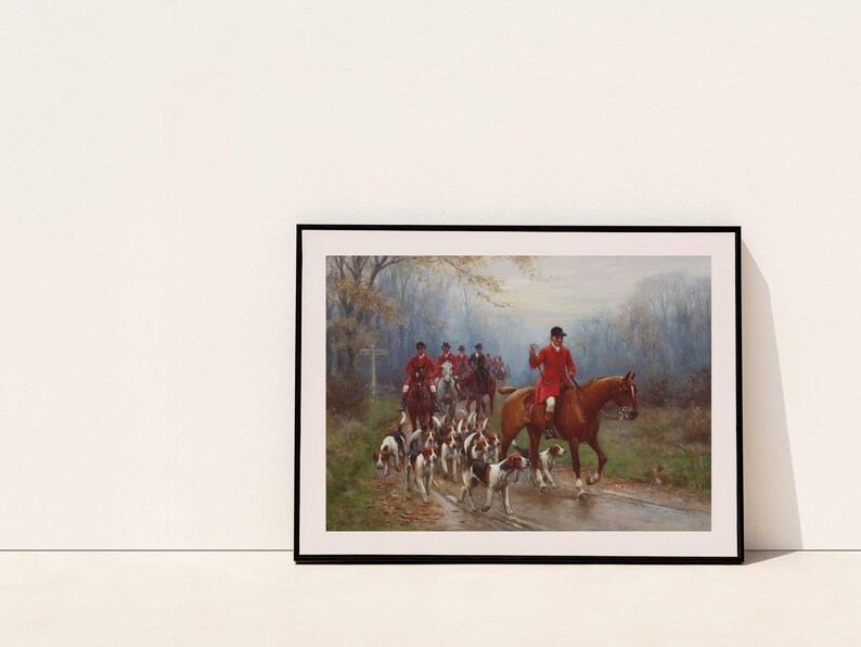 May include: Framed print of a hunting scene. A group of riders in red coats on horseback lead a pack of hounds along a path. The artwork has a classic, traditional style, with muted colors and a focus on the riders and dogs.