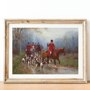 May include: Framed print of a hunting scene. A group of riders in red coats on horseback are followed by a pack of hounds. The artwork is set in a wooded area with a road, and the overall color palette is muted with greens, browns, and grays.