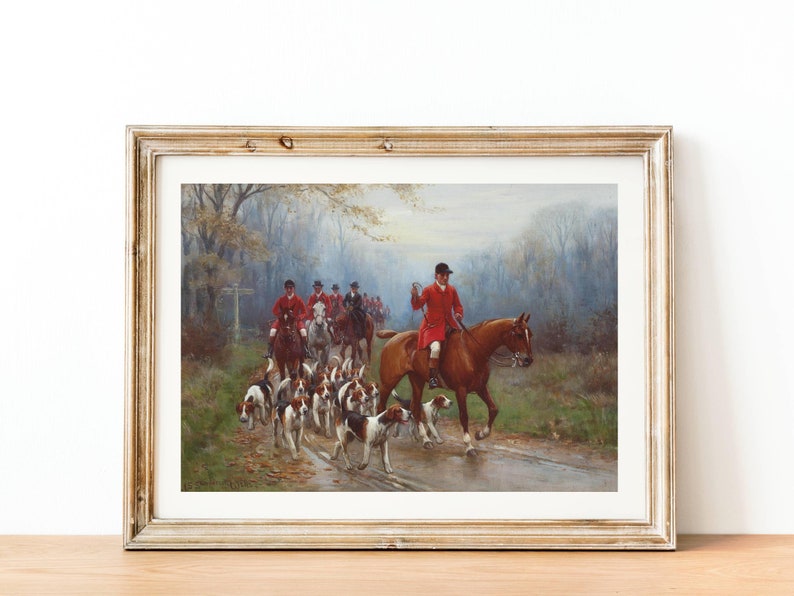 May include: Framed print of a hunting scene. A group of riders in red coats on horseback are followed by a pack of hounds. The artwork is set in a wooded area with a road, and the overall color palette is muted with greens, browns, and grays.