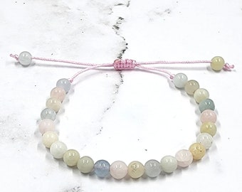 May include: A delicate bracelet made with pastel-colored beads and a pink cord. The bracelet is adjustable with a sliding knot.
