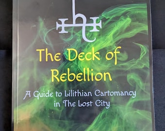 May include: A book titled "Oracle of the Dae: The Deck of Rebellion" with a green and black background. The cover features a stylized symbol and the author's name, Tava Baird.